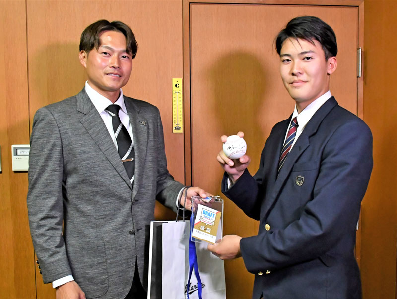 千葉ロッテからドラフト４位指名のあいさつを受け、有吉優樹スカウト（左）から吉井理人監督のサインボールなどを受け取った幕張総合高の早坂響投手＝３０日、千葉市美浜区