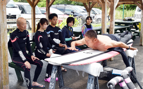 山本さん(右)からボードのこぎ方を教わる記者=一宮町のサーフショップ「HIC」