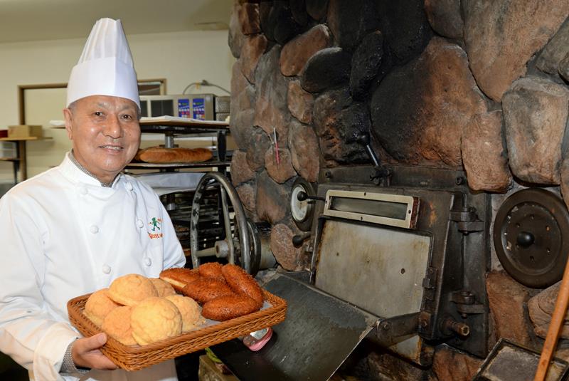 自慢の石窯の前で、人気商品のメロンパン、カレーパンを紹介する創業者の横手会長＝船橋市海神のピーターパン石窯パン工房店