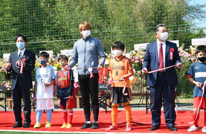 人工芝グラウンドのオープンイベントでテープカットするカレンさん（右から４人目）と岡田町長（同２人目）ら＝１１日、栄町請方