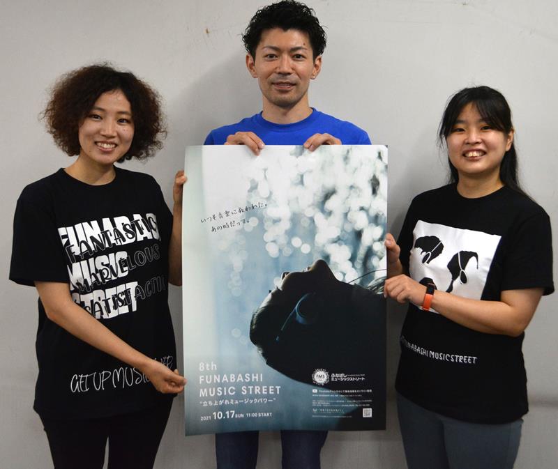 「ふなばしミュージックストリート」のポスターで視聴を呼び掛ける実行委の小松さん（中央）、濱津さん（左）、三宅風優さん。着ているのはネット販売もする今年のオリジナルＴシャツ＝船橋市内