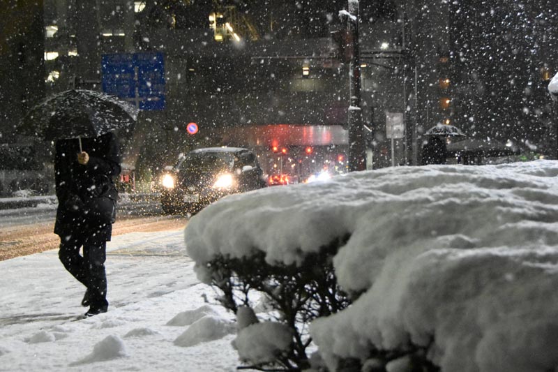 雪が降り積もる中、千葉都市モノレール県庁前駅近くを歩く人＝６日午後６時４０分ごろ、千葉市中央区