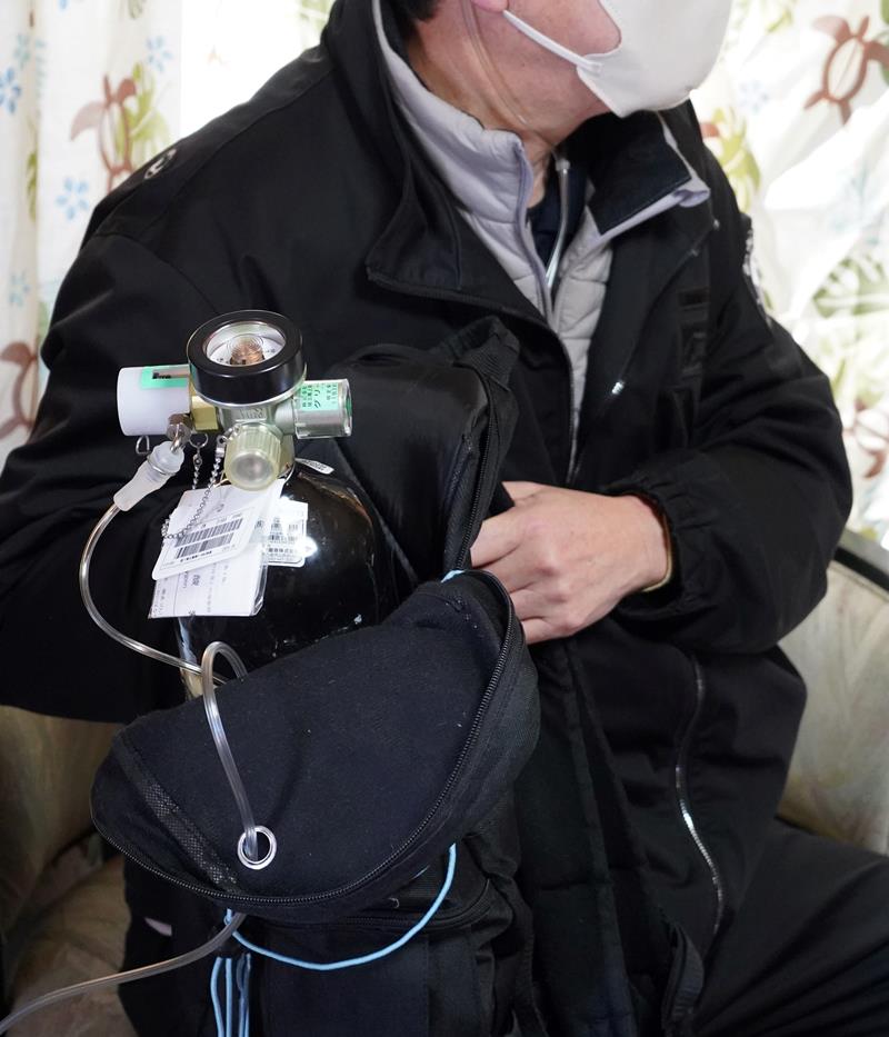 新型コロナ感染で肺に障害が残り、酸素ボンベを抱える男性＝２１日、いすみ市