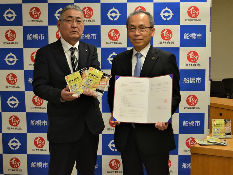 船橋産の米で試作した非常食「玄米がゆ」を手にする石井食品の久保取締役(左)と松戸市長=7日、船橋市役所