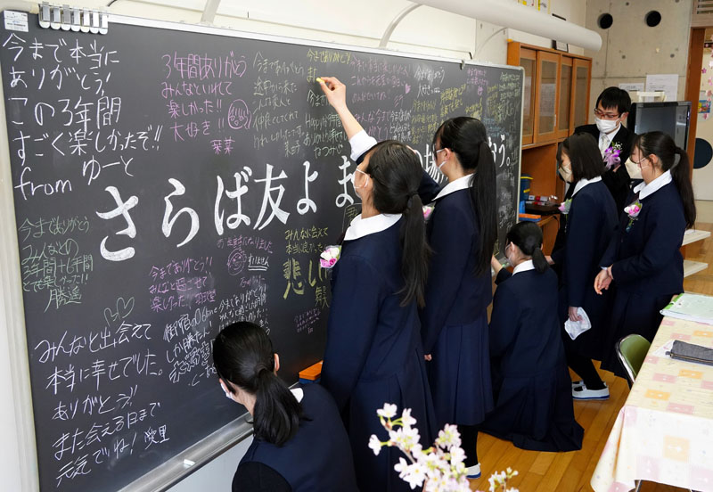 黒板に寄せ書きする卒業生