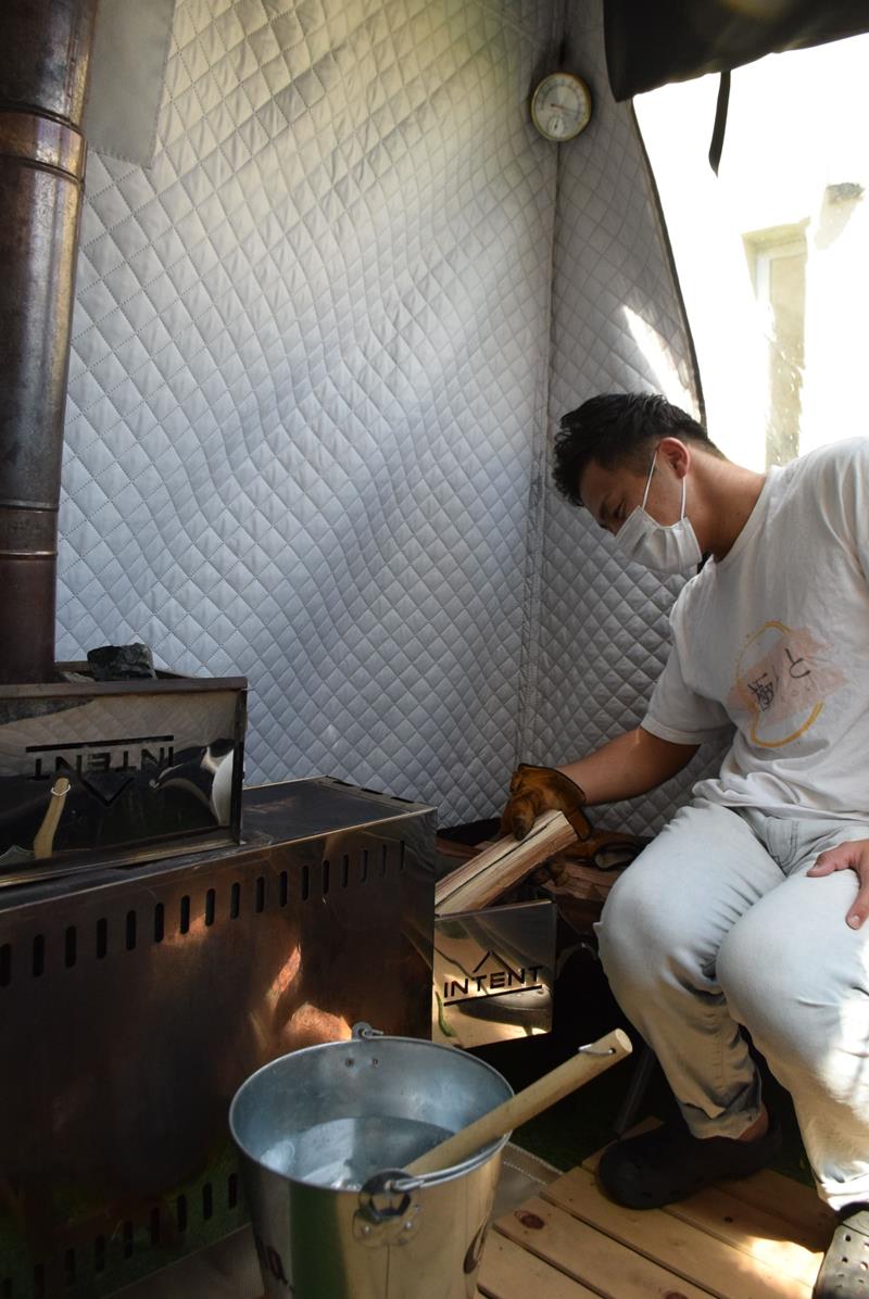 テント内でストーブにまきを入れる望月さん