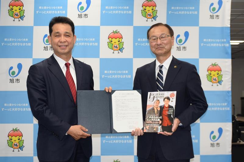 協定書とロケ地情報誌を手にする藤崎社長（左）と米本市長＝旭市役所