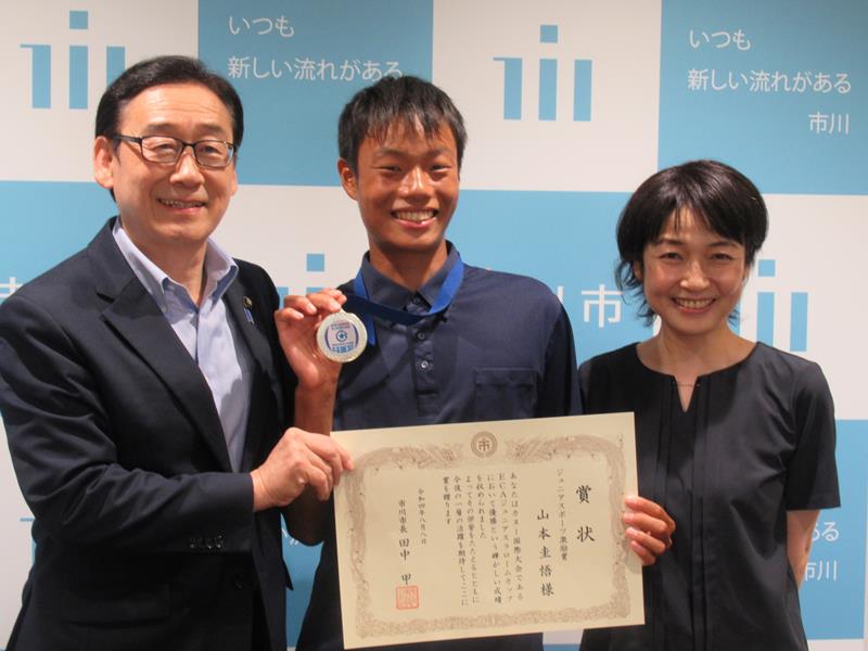 優勝メダルを掲げる山本さん（中央）。左は田中市長、右は母親のことみさん＝市川市役所