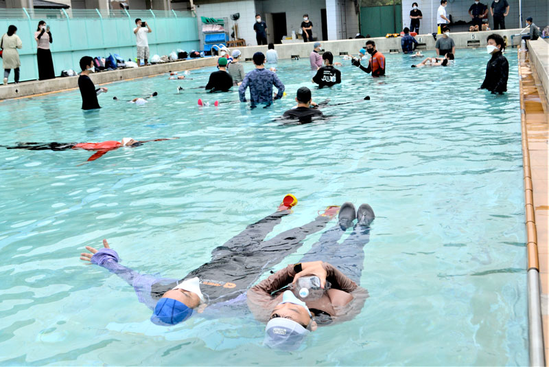 服や靴を身に着けたままプールに入り、ペットボトルも活用して浮く方法を海保職員から教わる親子=船橋市