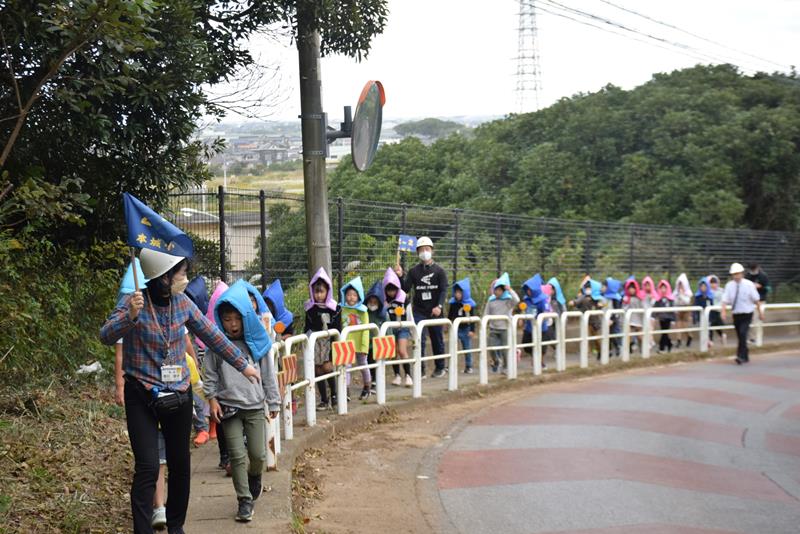 高台の避難場所を目指して歩く防災頭巾姿の児童たち＝銚子市