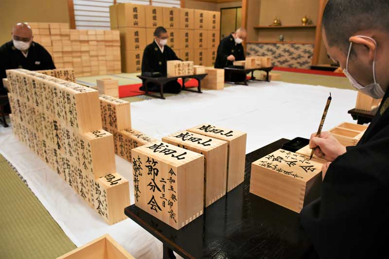 節分会の豆まきで使用する福枡に筆を入れて仕上げていく成田山新勝寺の僧侶＝１１日、成田市