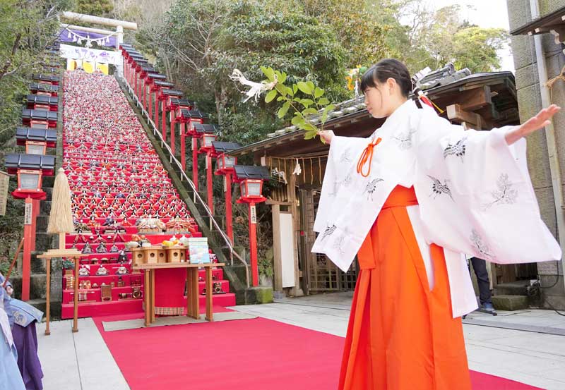 約１８００体のひな人形が飾られた石段６０段の前で舞を披露する遠見岬神社の小林美咲さん＝１１日、勝浦市