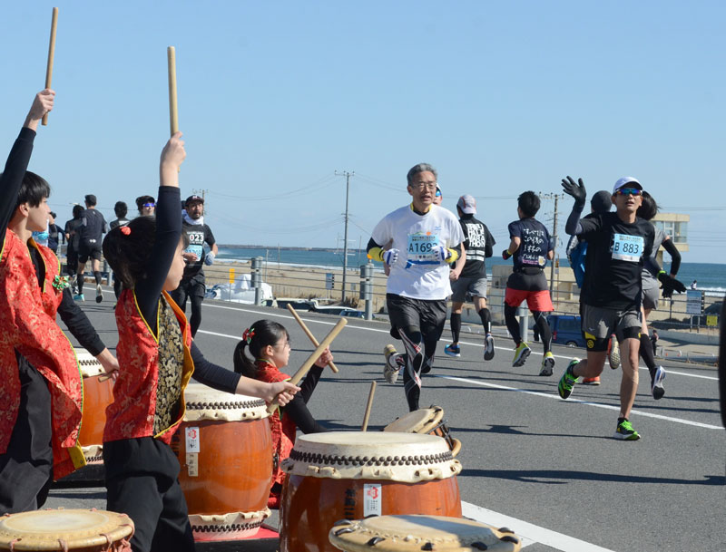地元の太鼓演奏チームの応援を受けながら、九十九里有料道路を走る参加者＝九十九里町