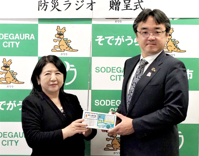 防災ラジオを寄贈する石村社長（左）と粕谷市長＝袖ケ浦市
