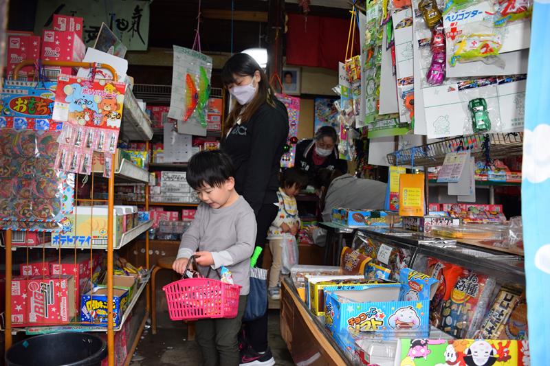 ずらりと並ぶ駄菓子からお気に入りを選び、かごに入れる子どもたち