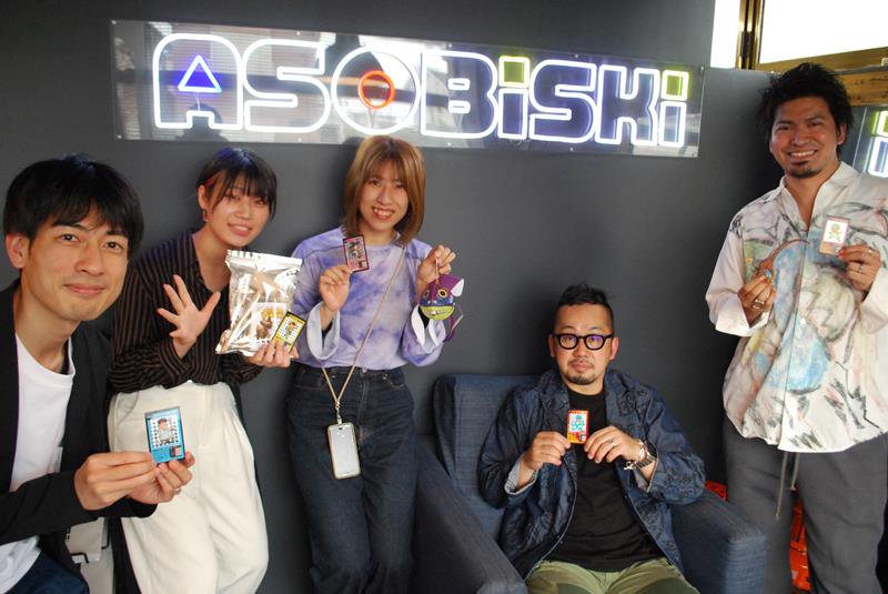 遊び心満載の名刺やワークショップ素材を披露する社員。右から2人目は近藤代表=習志野市のアソビスキー社内