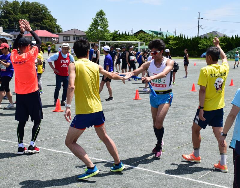 仲間を拍手で迎え、たすきをつなぐランナーたち＝４日、茂原市立二宮小グラウンド