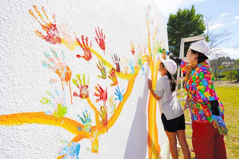 バルサミコヤスさん(右)と一緒にカラフルな手形を押す児童=23日、勝浦市立総野小