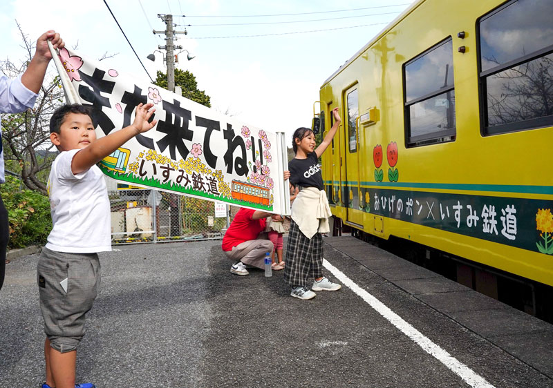 列車を見送るいすみ鉄道一日社長の中村梨乃さん(中央)と真那杜君=大多喜駅