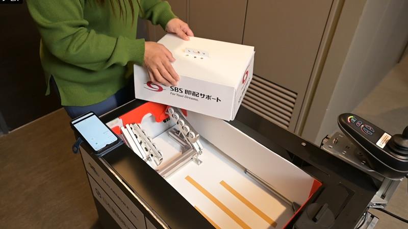 地上配送ロボットが届けた荷物を玄関先で住人が受け取る様子（市提供）