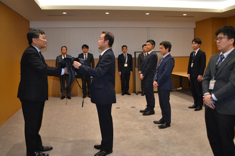 ヘルメットや軍手など被災地支援に必要な物品が入ったリュックを、神谷市長(左)から受け取る市職員=5日、千葉市役所