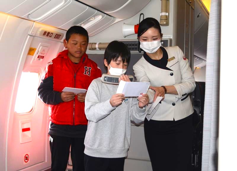 ＪＡＬ客室乗務員のサポートを受けて機内アナウンスに挑戦する児童＝１６日