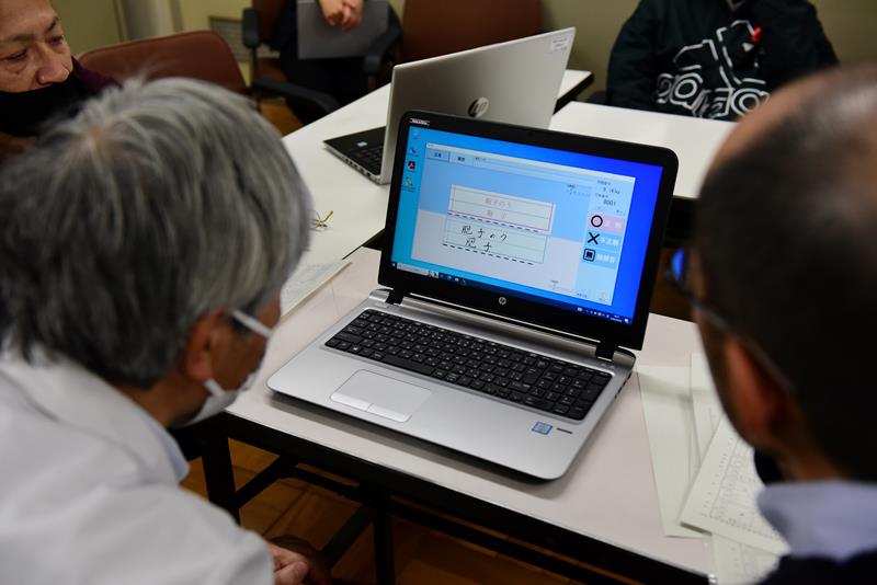 模範解答と照らし合わせて記述式の採点を行う教員