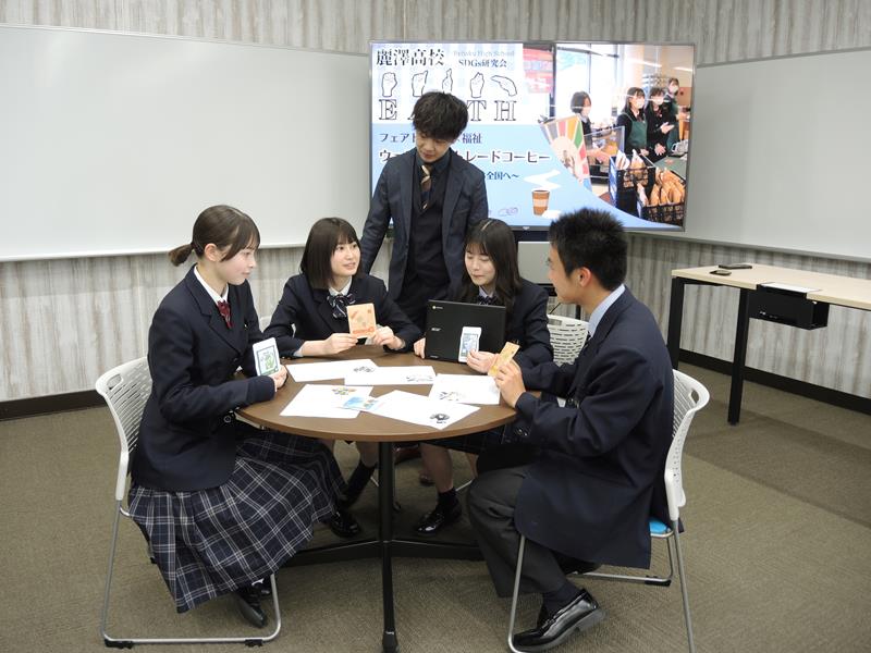 フェアトレードの商品を手にミーティングに臨む部員たち。(左から)ニュートンさん、薮崎さん。顧問の瀧村教諭が見守る=柏市、4月27日
