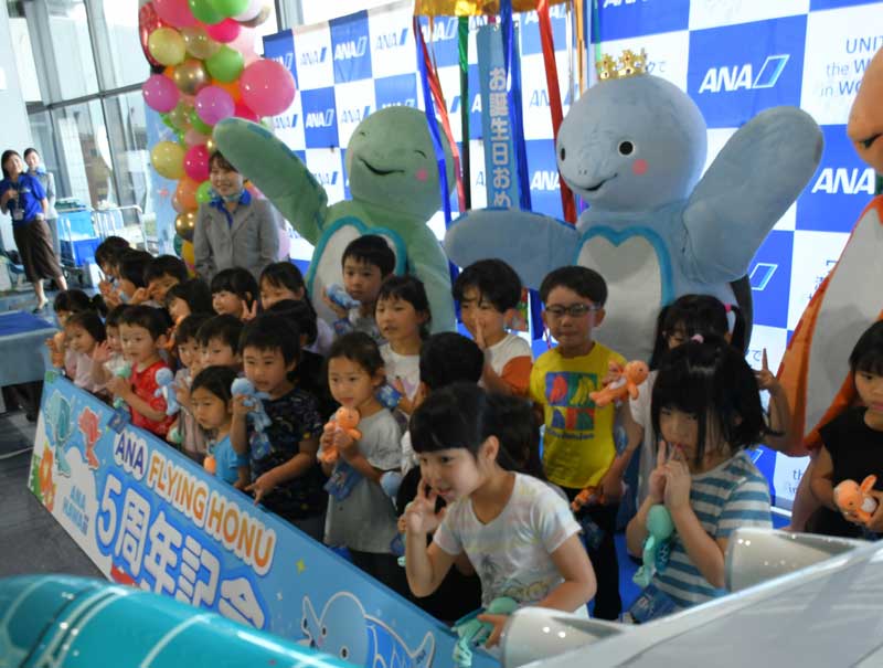 成田空港とハワイを結ぶ「フライングホヌ」初号機の就航5周年を着ぐるみとともに祝う園児たち=24日、成田市