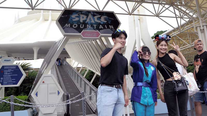 スペース・マウンテンの前で従業員と記念撮影する来園者＝３１日、浦安市の東京ディズニーランド
