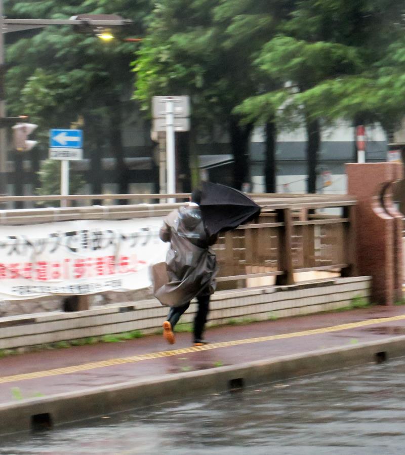 暴風雨の中を急いで歩く男性=16日午後5時50分ごろ、千葉市中央区