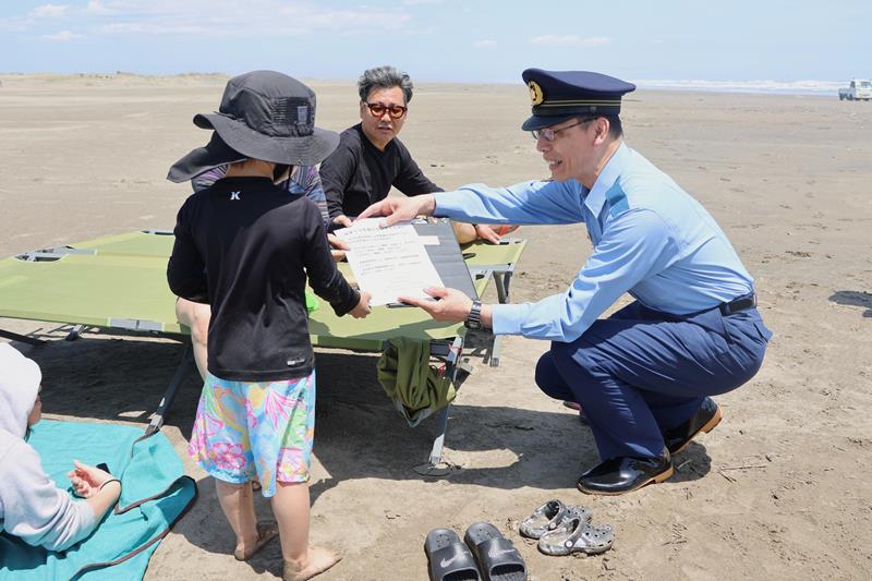 家族連れにビラを手渡す山武署の岡崎署長（右）＝３日、山武市の本須賀海岸