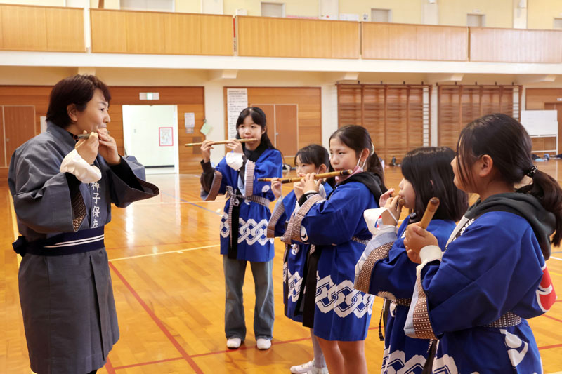 竹に穴を開けた笛を吹いて音出しに挑戦する児童
