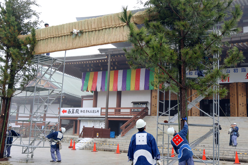 成田山新勝寺の大本堂前に大しめ縄と背の高い門松を飾る工務係員ら＝２５日、成田市