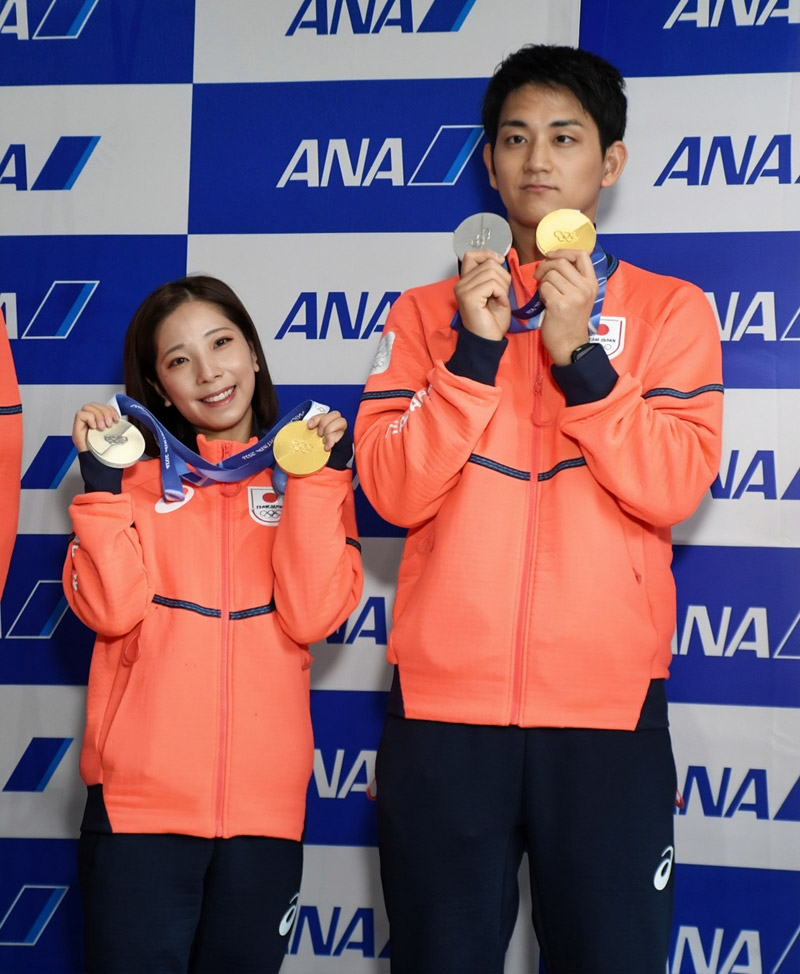 ミラノ・コルティナ冬季五輪で獲得した金と銀のメダルを成田空港で掲げるフィギュアスケートペアの(左から)三浦選手と木原選手=24日午後、成田市